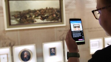 Frau hält Smartphone mit Museumsguide vor Gemälde in Ausstellung