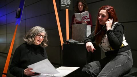 Zwei Frauen lesen Informationsmaterialien, eine hört am Telefon zu.