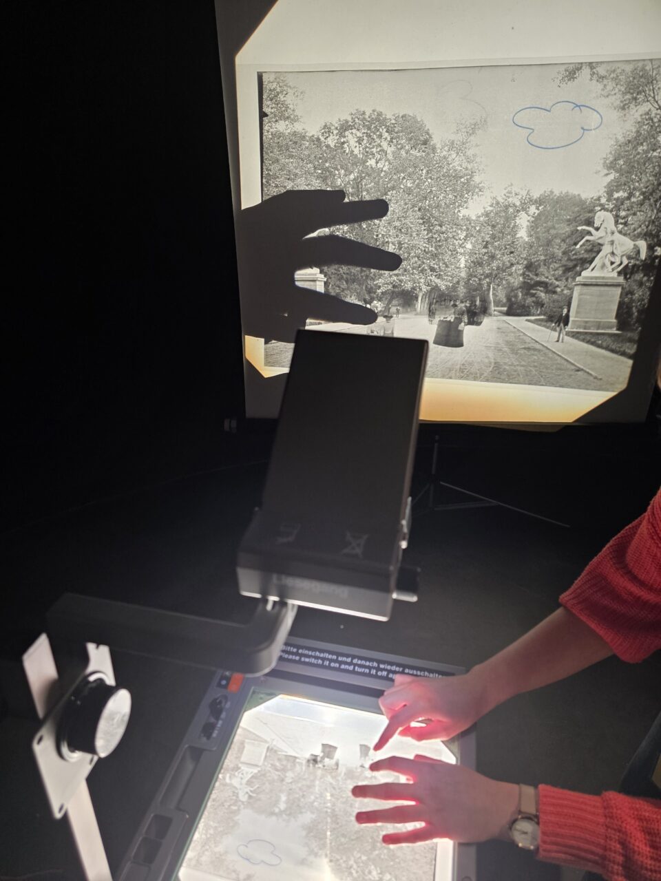 Hände verschieben auf einem Projektor Elemente eines historischen Fotos von einem Park.