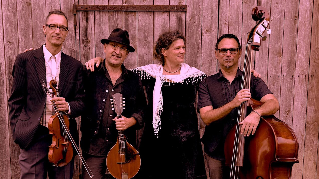 Vier Musiker der Gruppe Pankraz mit Instrumenten vor Holzwand