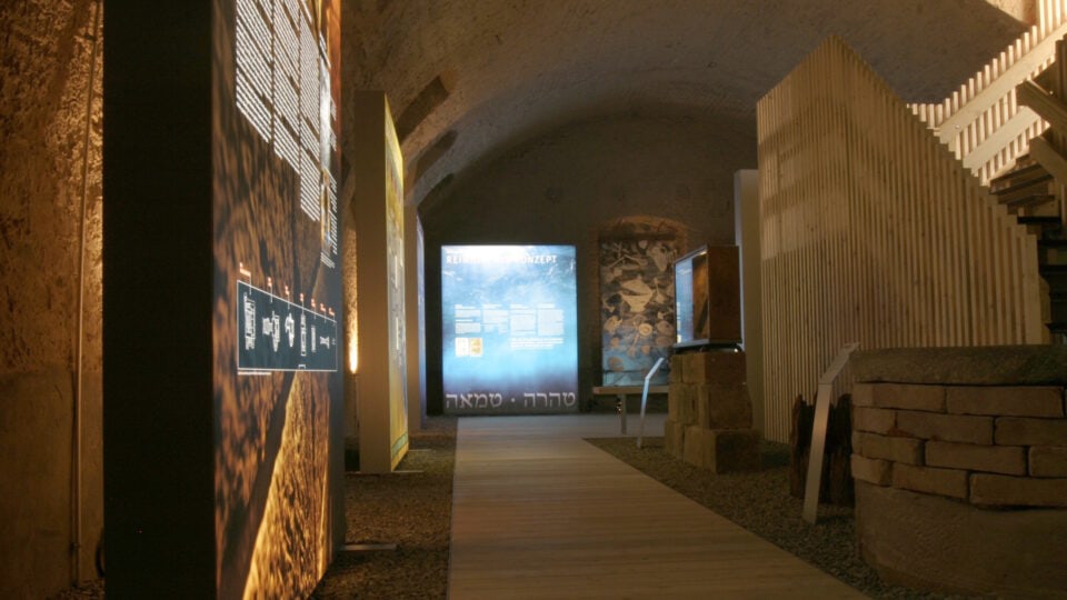 Ein Holzsteg führt an Objekten und Tafeln vorbei durch die Ausstellung Vom Bad zum Brunnen